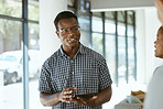 Young happy african american businessman holding a digital tablet while talking with colleagues in an office at work. Male boss wearing glasses and talking to coworkers in a meeting at work