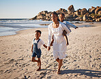 Portrait of a beautiful young african american mother at the beach with her two children. Little girl sitting on her moms back while her brother holds her hands as they walk along the beach