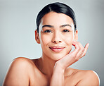 Portrait of a beautiful mixed race woman with smooth soft skin in a studio. Hispanic model with healthy natural glowing skin looking confident against grey copyspace while doing routine skincare