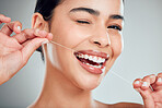 Studio portrait of a smiling mixed race young woman with glowing skin posing against grey copyspace background while flossing her teeth for fresh breath. Hispanic model using floss to prevent a cavity