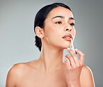 A beautiful young mixed race woman with glowing skin posing against grey copyspace background. Hispanic woman applying lipstick in a studio