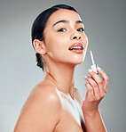 Portrait of a beautiful confident young mixed race woman with glowing skin posing against grey copyspace background. Hispanic woman applying lipstick in a studio