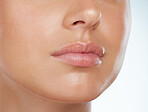 Closeup of perfect lips on unknown woman in studio. Caucasian model with smooth glowing skin isolated against a grey background and posing. Woman with healthy luscious plump lips and routine lip care