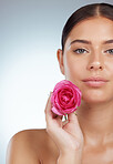 Closeup portrait of beautiful woman holding pink rose while posing topless with copyspace. Caucasian model isolated against grey studio background with smooth skin, delicate healthy skincare routine