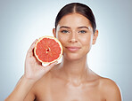 Portrait of beautiful woman holding grapefruit while posing topless with copyspace. Caucasian model isolated against grey studio background with smooth glowing skin, fresh healthy skincare routine