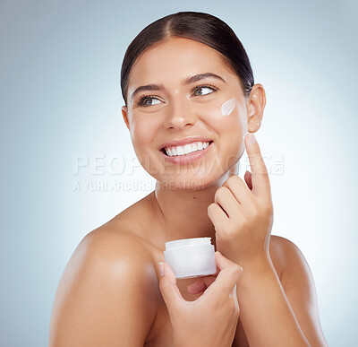 Buy stock photo Smiling beautiful woman applying face cream while posing with copyspace. Caucasian model isolated against grey studio background with product on cheek. Moisturise and sunscreen for healthy skincare