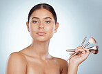 Portrait of beautiful woman holding cosmetic makeup brushes while posing with copyspace. Caucasian model isolated against a grey studio background. Getting ready to apply makeup in skincare routine