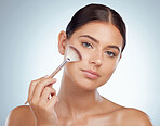 Portrait of beautiful woman using cosmetic makeup brush to apply highlighter makeup while posing with copyspace. Caucasian model isolated against grey background. Getting ready after skincare routine