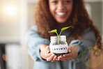 Young african american woman presenting her glass savings jar with a budding plant growing out from it at home. Happy mixed race person smiling while planning, saving and investing for her future