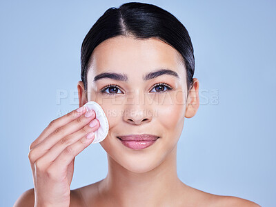 Buy stock photo Studio Portrait of a beautiful mixed race woman using a cotton pad to remove makeup during a selfcare grooming routine. Hispanic woman applying cleanser to her face against blue copyspace background