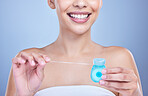 Closeup of a smiling mixed race young woman with glowing skin posing against blue copyspace background while flossing her teeth for fresh breath. Hispanic model using floss to prevent a cavity