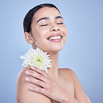 A beautiful mixed race woman posing with a flower. Young hispanic using an organic skincare treatment against a blue copyspace background