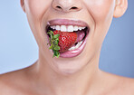 A happy smiling mixed race woman eating a strawberry. Hispanic model promoting the skin benefits of a healthy diet against a blue copyspace background