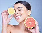 A happy smiling mixed race woman holding a lemon and grapefruit. Hispanic model promoting the skin benefits of citrus against a blue copyspace background