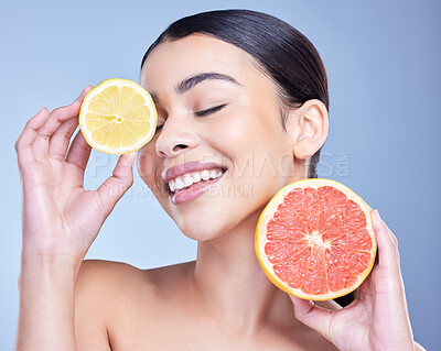 Buy stock photo A happy smiling mixed race woman holding a lemon and grapefruit. Hispanic model promoting the skin benefits of citrus against a blue copyspace background