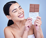 A beautiful mixed race woman holding a slab of chocolate. Hispanic model snacking on dessert against a blue copyspace background