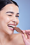 Studio portrait of a beautiful mixed race woman holding a slab of chocolate. Hispanic model snacking on dessert against a blue copyspace background