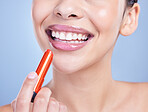 Closeup of a beautiful young mixed race woman with glowing skin posing against blue copyspace background. Hispanic woman applying lipstick in a studio