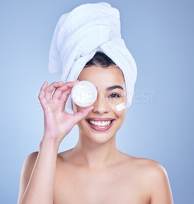 Buy stock photo Studio Portrait of a beautiful smiling mixed race woman applying cream to her face. Hispanic model with glowing skin holding moisturiser against a blue copyspace background