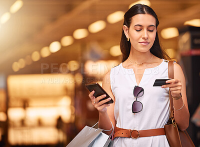 Buy stock photo A young mixed race woman using a cell phone and bank card while carrying bags during a shopping spree. Young brunette woman purchasing items online with her smartphone and credit card in a shopping mall. A little retail therapy is never a bad idea