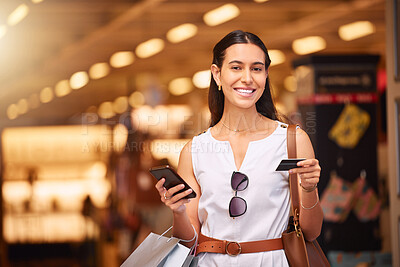Buy stock photo Portrait of young mixed race woman using a cell phone and bank card while carrying bags during a shopping spree. Young woman purchasing items online with her smartphone and credit card in a shopping mall. 