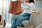 Woman folding a pair of shorts. Woman relaxing at home cleaning clothing. Woman sitting in a chair folding laundry. Woman doing housework chores at home cropped. Mixed race woman folding neat clothing