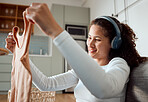 Young woman enjoying music and housework. Hispanic woman looking at a clean tshirt. Smiling woman enjoying her chore routine. Young woman using headphones for music. Woman folding a washed top