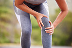 Active woman holding her leg in pain while exercising outdoors. Closeup of an athlete suffering with a painful knee injury, causing discomfort and strain.  Muscle sprain from a fractured joint