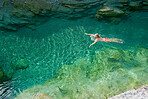 Overhead of a young woman on an adventure, swimming in an exotic blue river. Woman having fun relaxing in a lake on a travel vacation from above