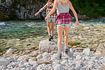 Unrecognizable friends crossing a river on a travel adventure exploring nature together. Closeup of two women walking across rocks in a lake, having fun on a summer vacation