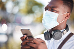 Handsome young african american man wearing mask and using his phone with wireless headphones around his neck. Adjusting to life during the corona virus pandemic. Taking precautions against covid 19
