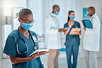 Young african american female doctor working on a digital tablet and wearing a mask while working at a hospital with colleagues. Black female nurse doing research on a digital tablet at work at a clinic
