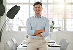 Young caucasian businessman standing with his arms crossed in an office alone at work. Headshot of one happy male businessperson smiling while standing at work