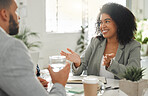 Businesspeople talking in a meeting together at work. Business professionals talking and planning in an office. Young mixed race  businesswoman with a curly afro explaining an idea to colleagues at a table