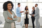 Young happy mixed race businesswoman standing with her arms crossed while in an office alone. One confident hispanic female boss with a curly afro standing in a meeting with coworkers