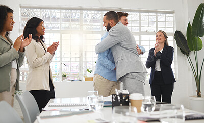Buy stock photo Happy businessmen hugging each other in support and unity while colleagues clap hands in a meeting at work. Diverse group of cheerful businesspeople welcoming an employee to their workplace together