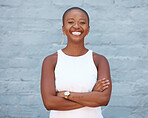 Cheerful bald african american woman looking confident while standing with her arms crossed outside against a brick wall. Carefree young woman smiling while looking at the camera 