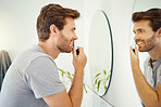 One handsome man trimming his nose hair  in a bathroom at home. Caucasian male using a nose trimmer while looking in a mirror in his apartment