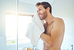 One handsome man washing his face in a bathroom at home. Caucasian male using a towel to dry his face and looking in a mirror in his apartment.