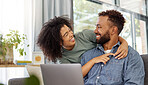 Mixed race couple smiling while using a laptop together at home. Cheerful hispanic boyfriend and girlfriend laughing while relaxing and using a laptop in the lounge at home