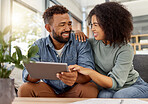 Happy young mixed race couple smiling while using a digital tablet together at home. Cheerful hispanic boyfriend and girlfriend laughing while relaxing and using social media on a digital tablet sitting on the couch in the lounge at home