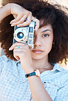 Young mixed race woman with curly hair taking creative photos on a vintage retro film camera. One female photographer looking in viewfinder while capturing pictures as a hobby or profession on a shoot