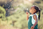 Happy little african american girl blowing a flower in outside. Cheerful child having fun playing and blowing a dandelion into the air in a park. Kid having fun with joy playing with a plant outdoors