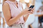 Close up of a business woman's hands using a smart phone in an office. Woman browsing on the internet, sending a text or using mobile app at her workplace