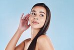 One beautiful young hispanic woman with healthy skin and sleek long hair posing against a blue studio background. Mixed race model with flawless complexion and natural beauty