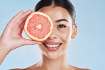 Beautiful young mixed race woman with a grapefruit isolated in studio against a blue background. Her skincare regime keeps her fresh. For glowing skin, eat healthy. Packed with vitamins and nutrients