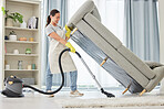 A mixed race domestic worker lifting and cleaning under the sofa. One mixed race female using a vacuum cleaning under a couch to begin spring cleaning