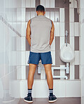 Back of athletic man urinating in a bathroom. Fit man taking a break from his workout to urinate in his gym toilet. Professional squash player taking a break to urinate
