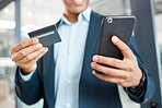 Closeup of a mixed race businessman holding and using a credit card and phone alone at work. One hispanic male businessperson making an online purchase with his debit card and cellphone