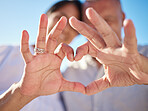 Affectionate mature mixed race couple sharing an intimate moment on the beach. Senior husband and wife making a heart shape with their hands. They love spending time together by the sea at sunset